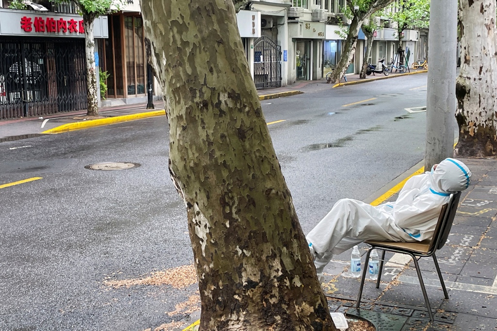 Een vermoeide medische werker zit langs een lege straat in Shanghai, China.