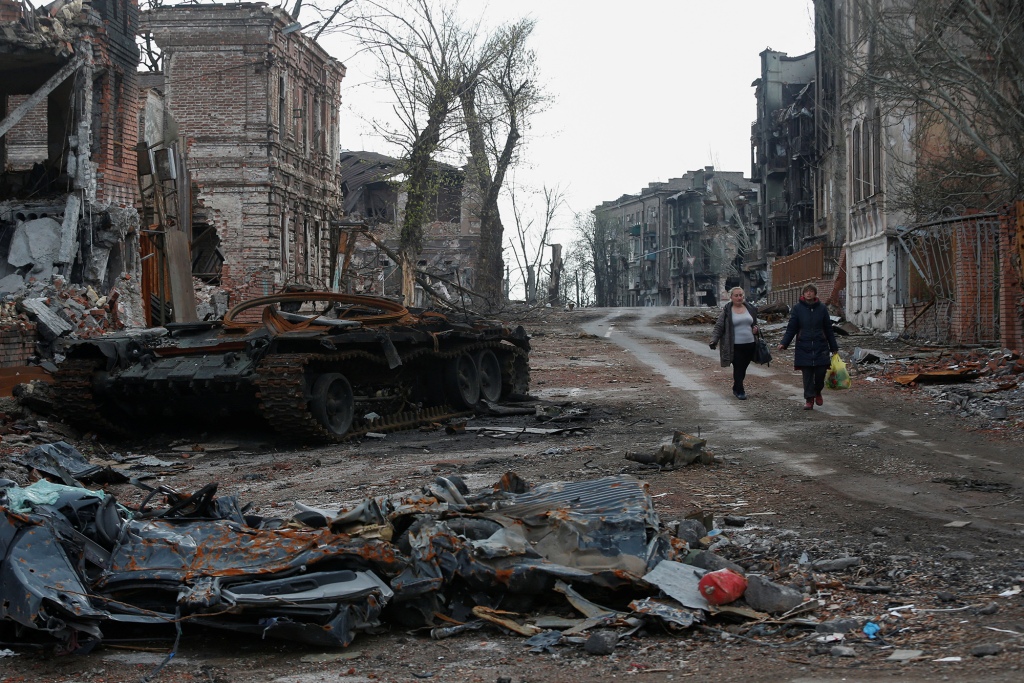 Mensen lopen in de buurt van een vernietigde tank en vernietigden gebouwen in de context van het conflict tussen Oekraïne en Rusland.