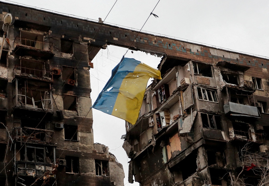 Een afbeelding van een gescheurde Oekraïense vlag hangt aan een draad voor een flatgebouw dat is verwoest tijdens het conflict tussen Oekraïne en Rusland in de zuidelijke havenstad Mariupol.