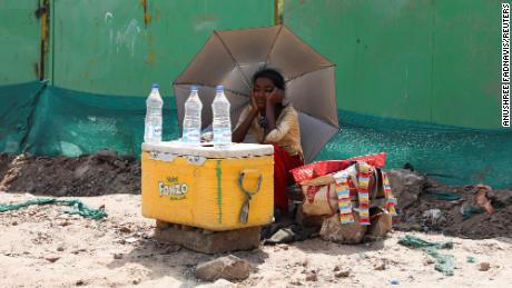 Een meisje dat water verkoopt, gebruikt een paraplu om zichzelf te beschermen tegen de zonnestralen in New Delhi.