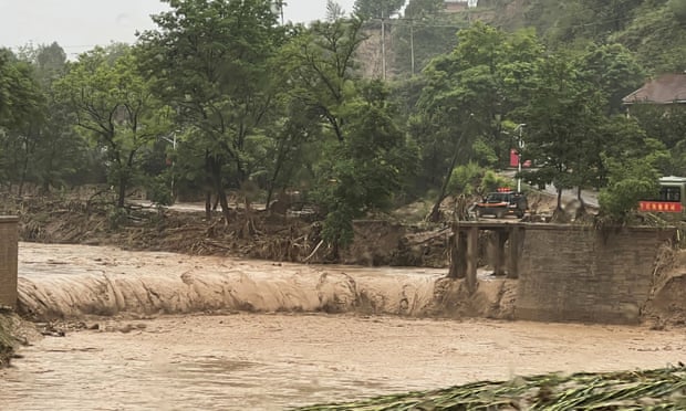 Een auto staat naast een deel van een brug die is weggespoeld door overstromingen in Qingyang, in het noordwesten van China