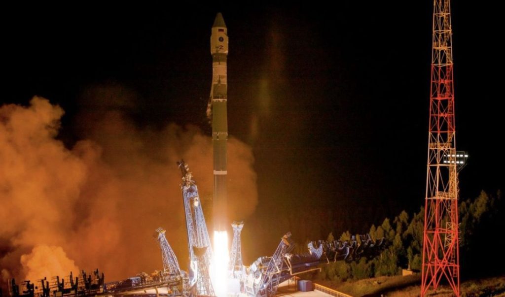 A Russian Soyuz rocket takes off at night, its exhaust plume glowing bright red.