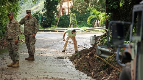 Troepen van de Nationale Garde leiden het verkeer terwijl inwoner Luis Nogueira helpt bij het opruimen van een weg die dinsdag is beschadigd door de orkaan Fiona in Cayai, Puerto Rico.